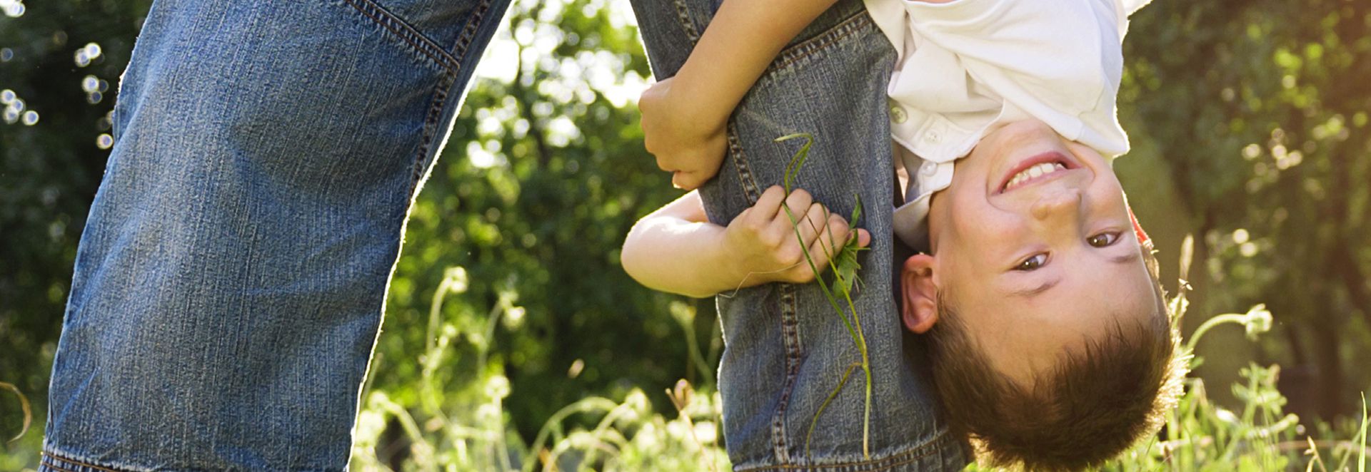 child hanging upside down while clinging to and adult's leg